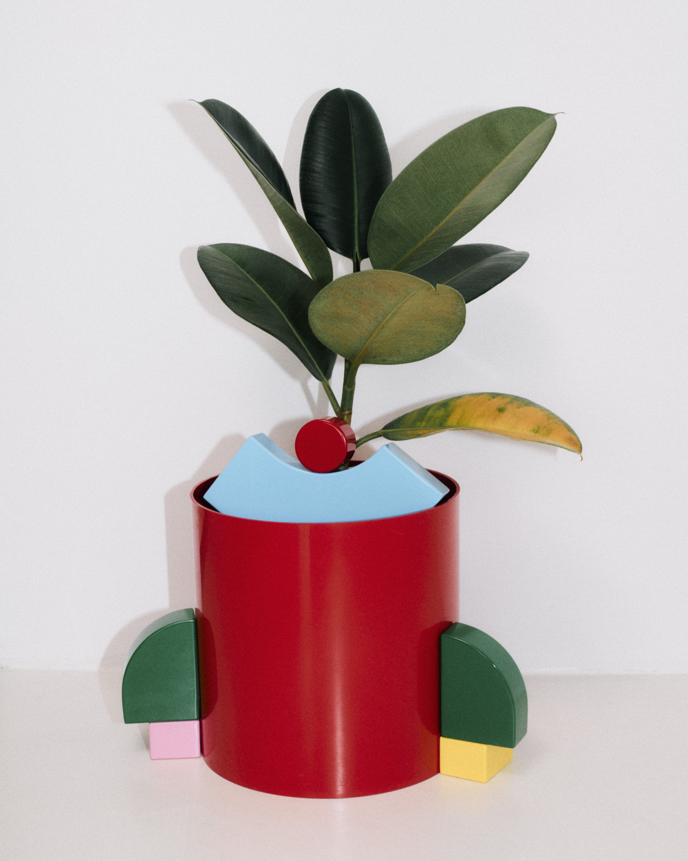 Colorful modular objects from the Little Family collection by nara.world arranged around a plant pot, creating a playful character-like composition